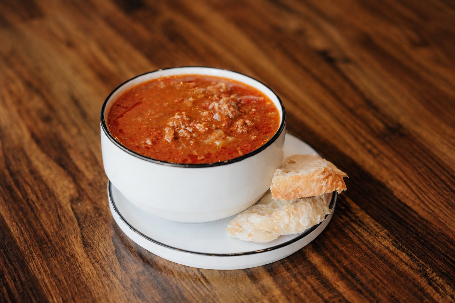 Signature beef chili in a white bowl with sourdough on a wooden table